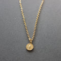 Gold necklace with a round pendant on a gray background