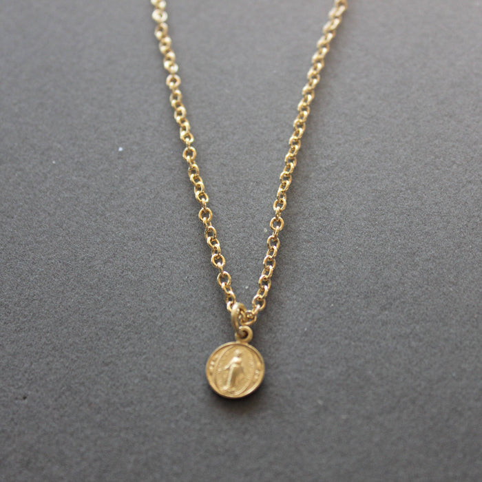 Gold necklace with a round pendant on a gray background