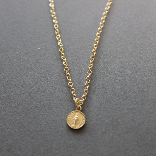 Gold necklace with a round pendant on a gray background