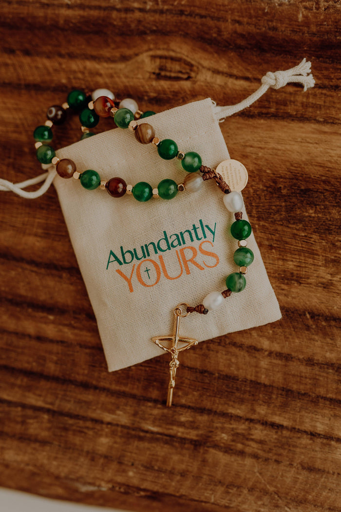 Green white and brown rosary with wooden background abundantly yours