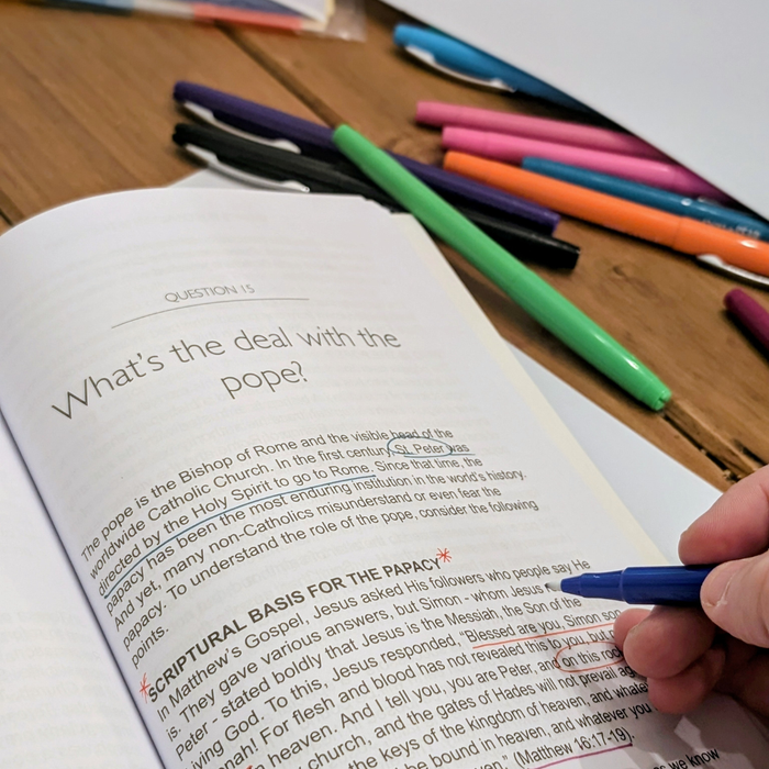 Open book with text and colorful pens on a wooden surface