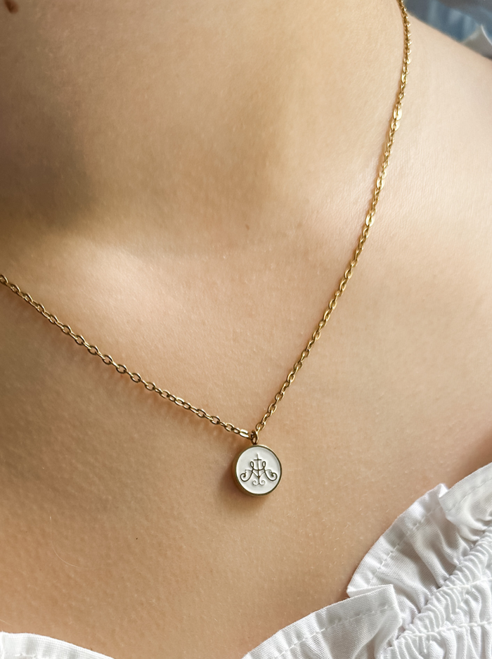 Ava Maria symbol on white background with gold border attached to golden chain on neck