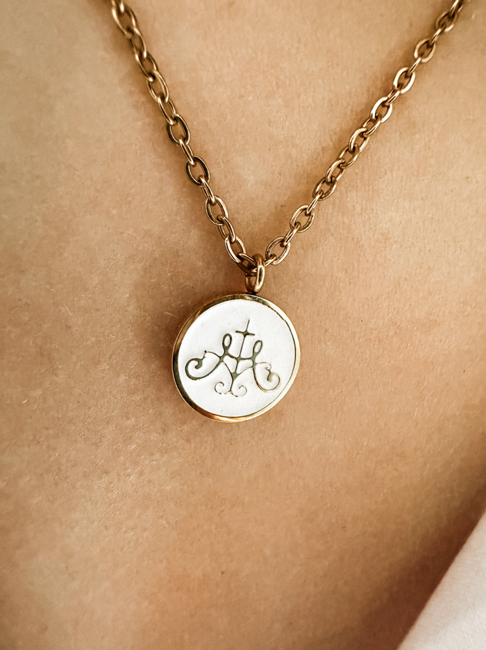 Ava Maria symbol on white background with gold border attached to golden chain on neck