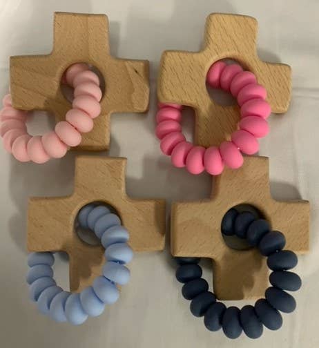 Four wooden cross-shaped teething rings with pink, blue, and navy silicone bands on a white background.