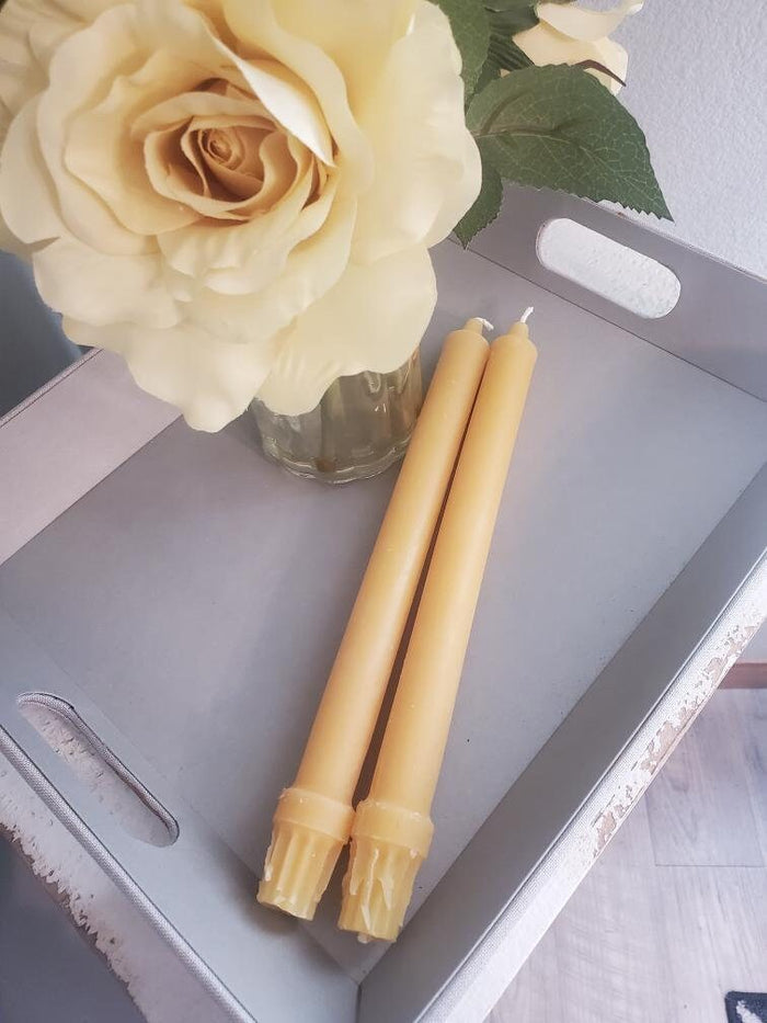 Two beeswax candles and a vase with white roses on a metal tray.