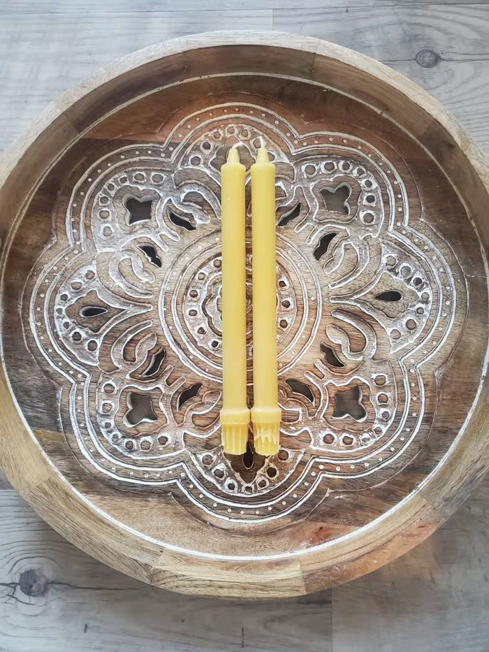 Decorative wooden bowl with intricate carvings and two yellow candles on a wooden surface.