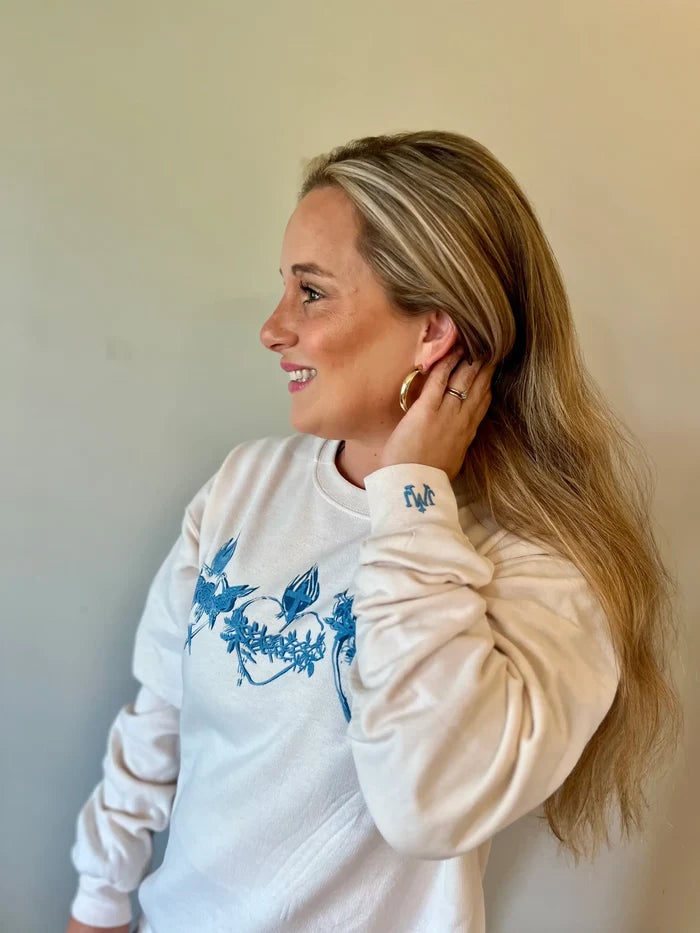 Woman wearing a white sweatshirt with blue floral design against a plain background