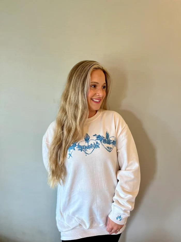 Woman wearing a white sweatshirt with blue designs against a plain background