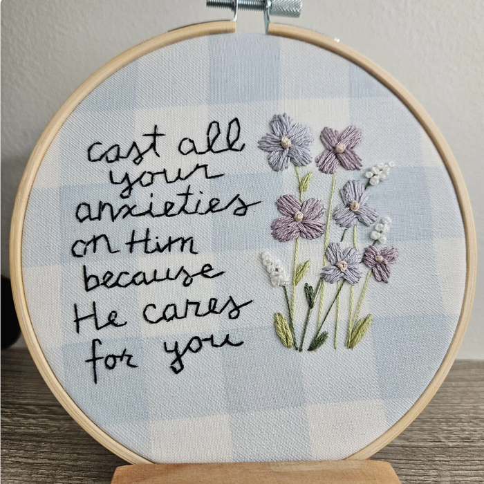 Embroidery hoop with floral design and text on a checkered background