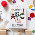 Catholic ABC Board Book surrounded by colorful blocks and toys on a white surface