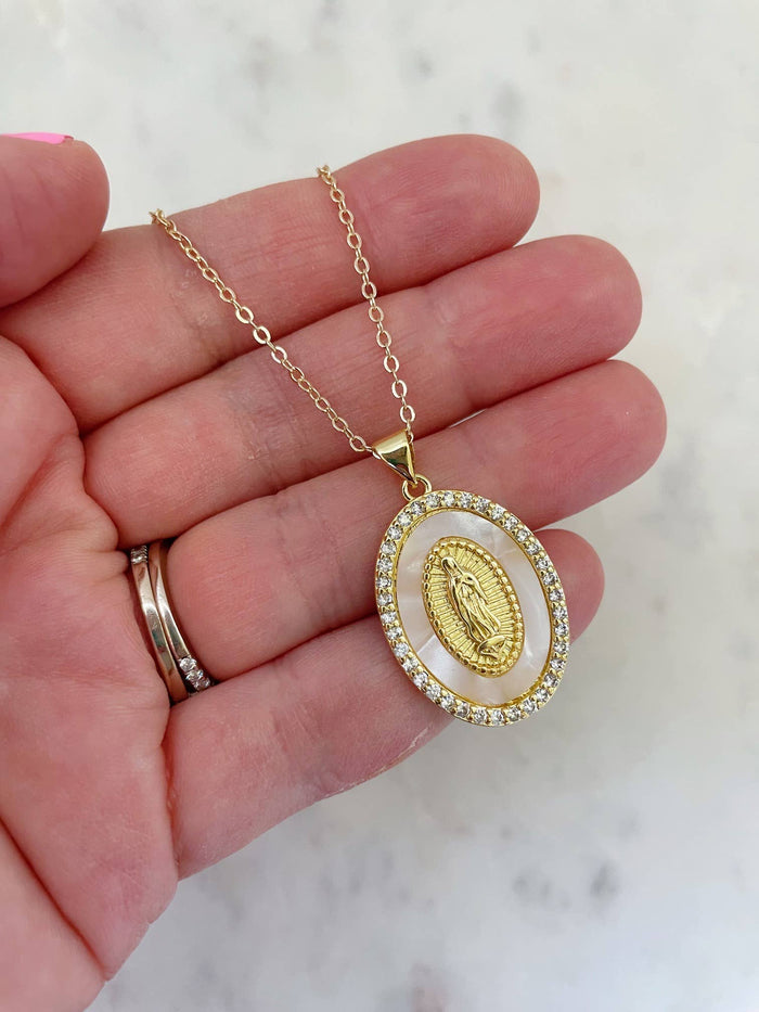 Gold necklace with a pendant held in a hand against a light background