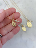 Gold necklaces with religious pendants held by a hand on a marble background
