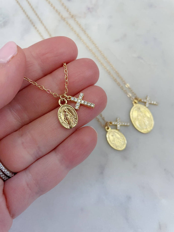 Gold necklaces with religious pendants held by a hand on a marble background