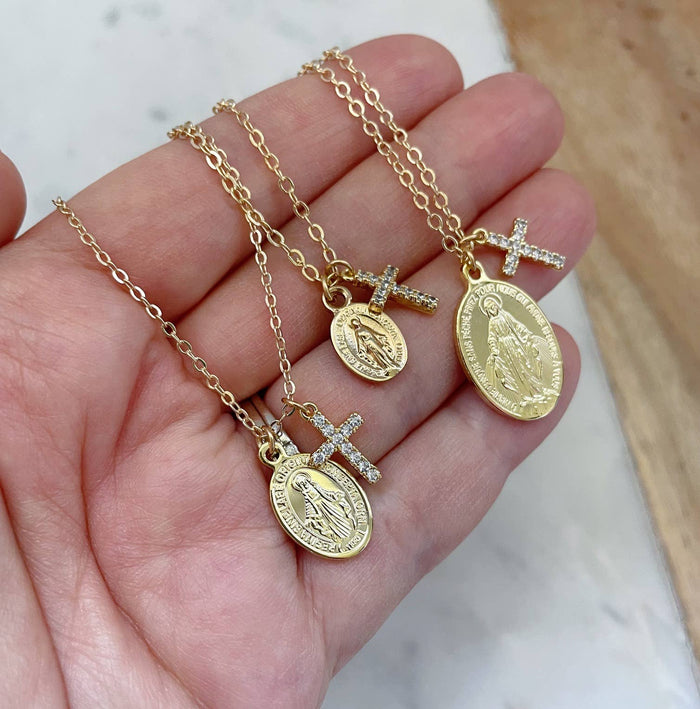 Gold necklaces with religious pendants on a hand against a neutral background
