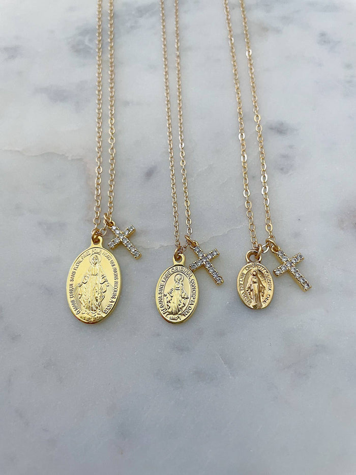 Three gold necklaces with religious pendants on a marble surface