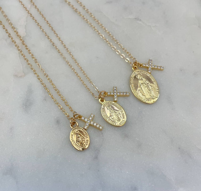 Three gold necklaces with religious pendants on a marble surface