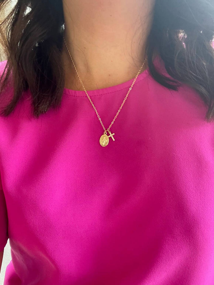 Person wearing a gold necklace with a pendant on a pink shirt