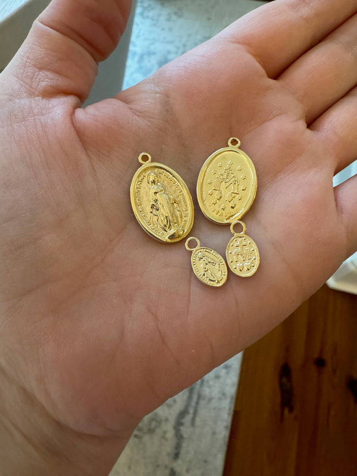 Four gold religious pendants on a person's hand with a blurred background.
