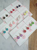 Set of earrings on branded cards with a floral design on a marble surface.