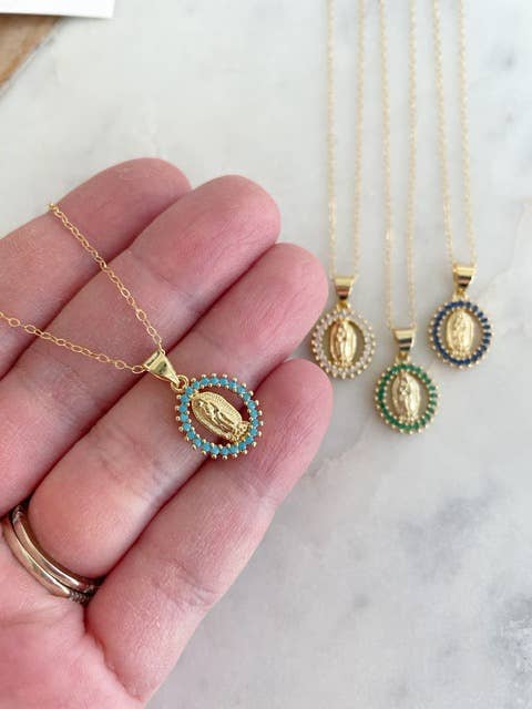Gold necklaces with pendants held by a hand on a marble surface