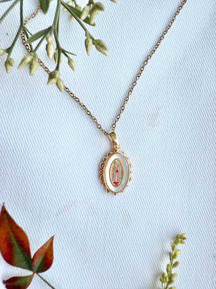 Gold necklace with a pendant on a light blue background with greenery