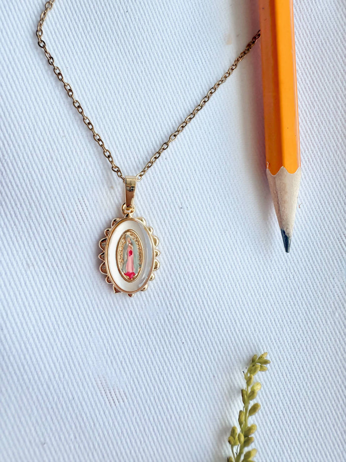 Gold necklace with a pendant on a white background with a pencil for scale.