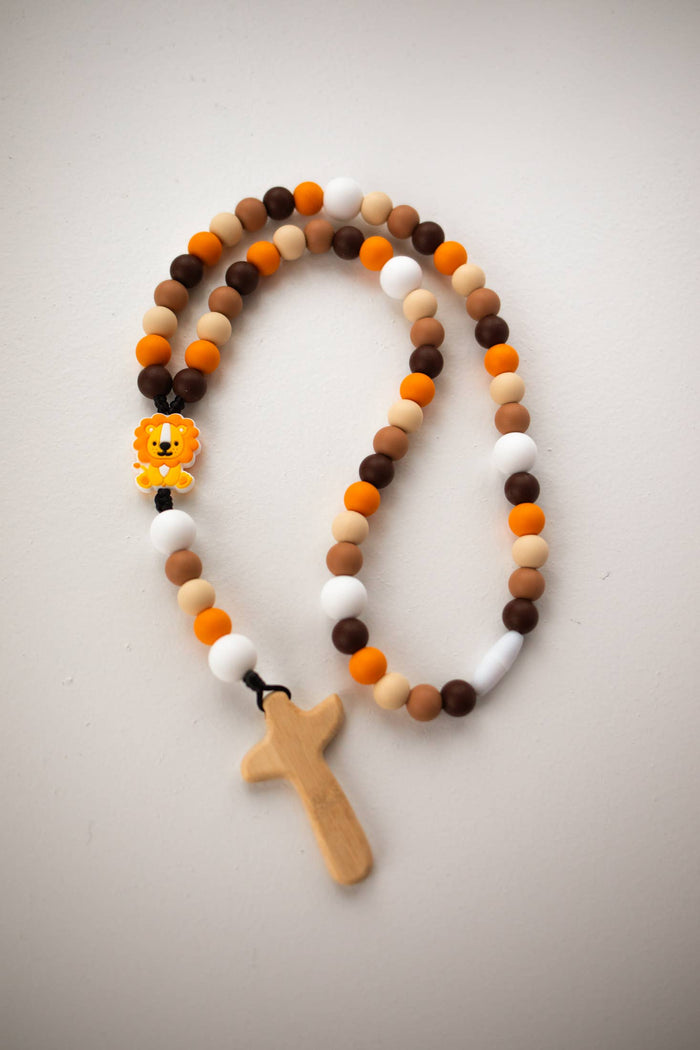 Beaded rosary with a cross and lion charm on a light gray background
