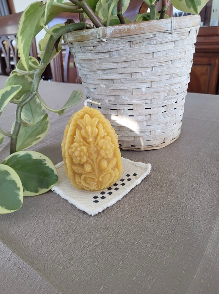 Decorative yellow candle with floral design on a white doily, next to a potted plant on a table.