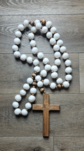 Wooden cross with white and brown beaded rosary on a wooden surface