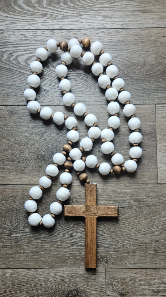 Wooden cross with white and brown beaded rosary on a wooden surface