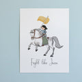 Print with illustration of Joan of Arc on horseback and 'Fight like Joan' text on a white surface.