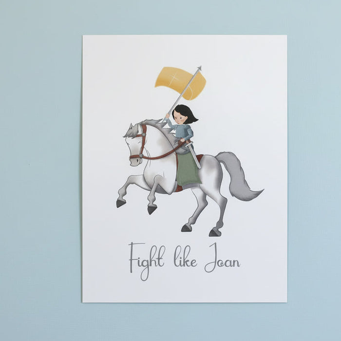 Print with illustration of Joan of Arc on horseback and 'Fight like Joan' text on a white surface.