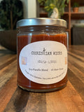 Jar of coffee candle by Christian Wicks on a wooden surface with a blurred background