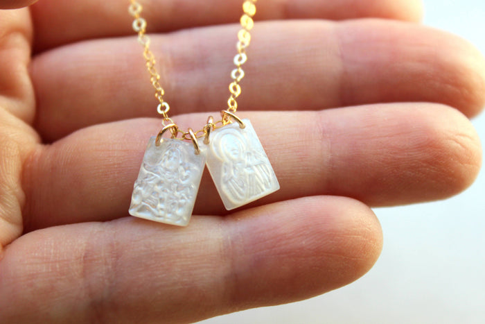 Gold chain with two white pendants held between fingers