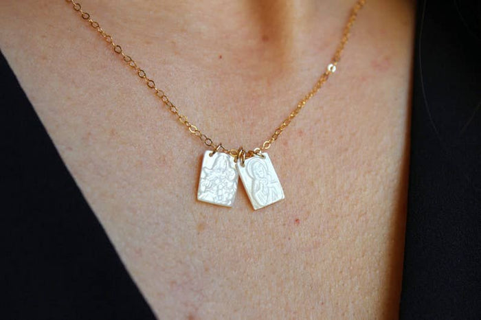 Gold necklace with two pendant tags on a person's neck against a black background