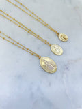 Gold necklaces with oval pendants on a marble surface