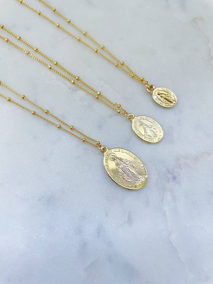 Gold necklaces with oval pendants on a marble surface