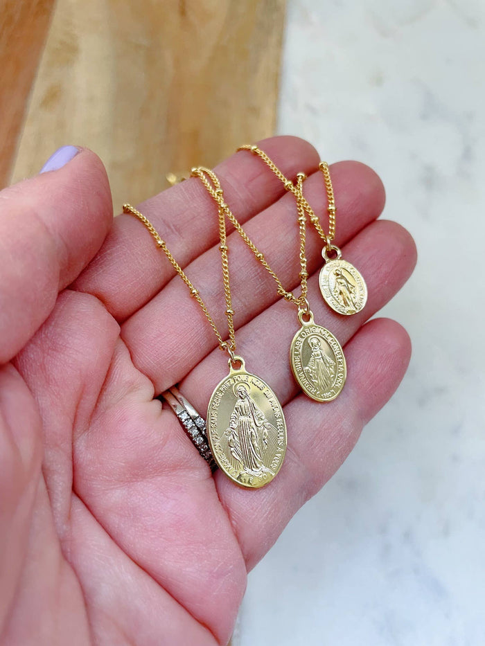 Three gold necklaces with religious pendants on a hand against a marble background