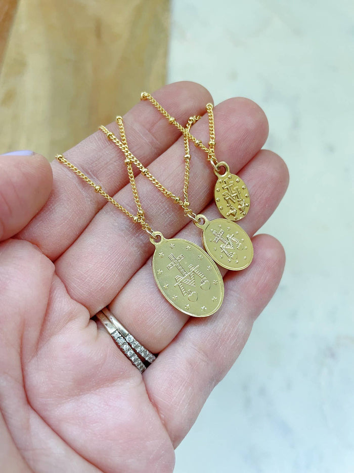Gold necklaces with pendants held in a hand against a neutral background