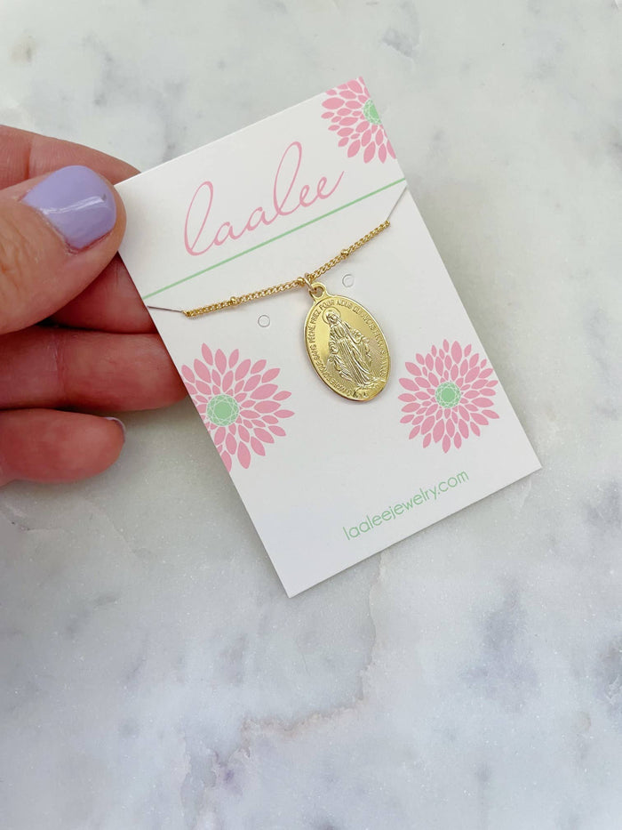 Gold necklace on a 'Laalee' branded card held by a hand with purple nail polish on a marble background.