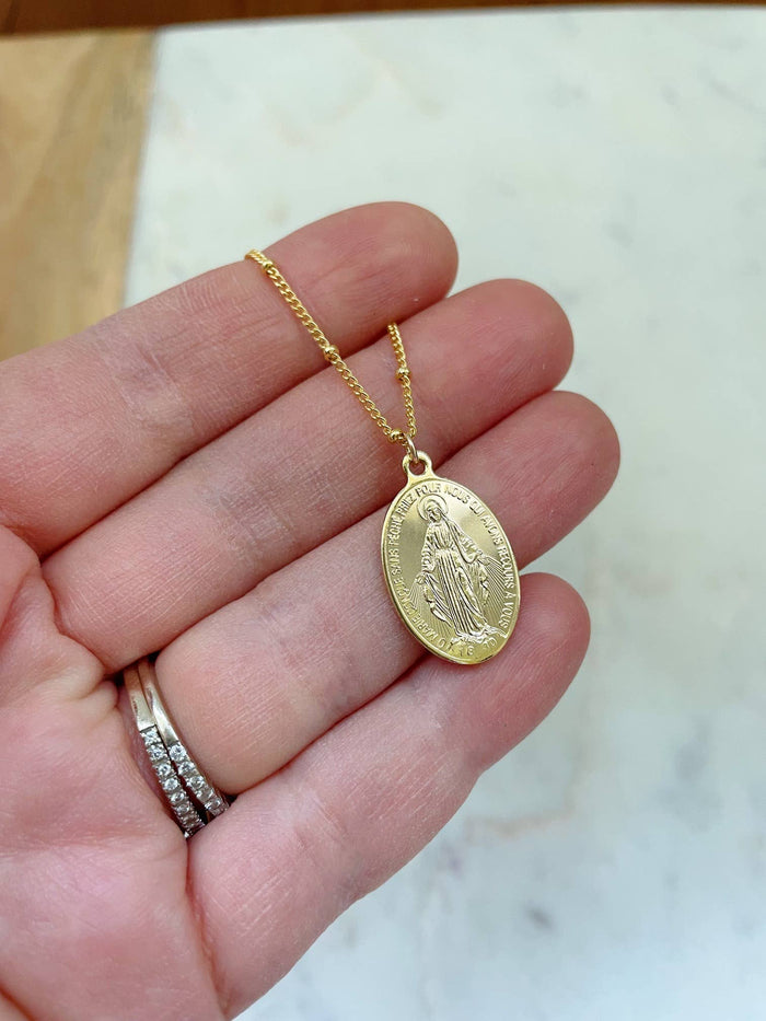 Gold necklace with a pendant held in a hand on a marble surface