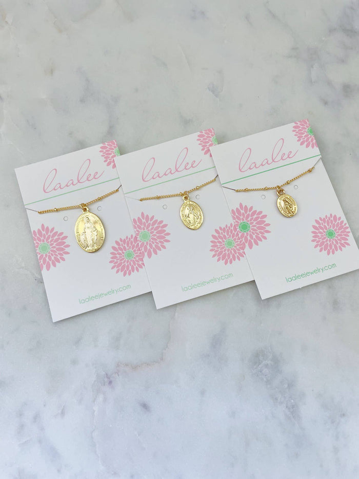 Three gold necklaces on 'Laalee' branded cards with pink floral designs on a marble surface.