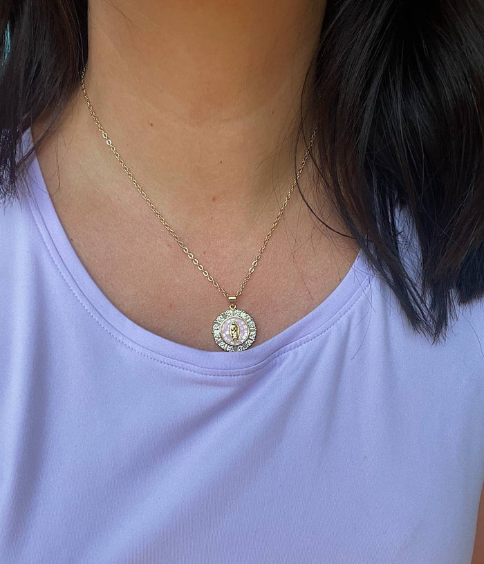 Necklace with a circular pendant worn by a person in a light purple shirt.