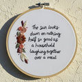 Embroidery hoop with floral design and text on a beige wall