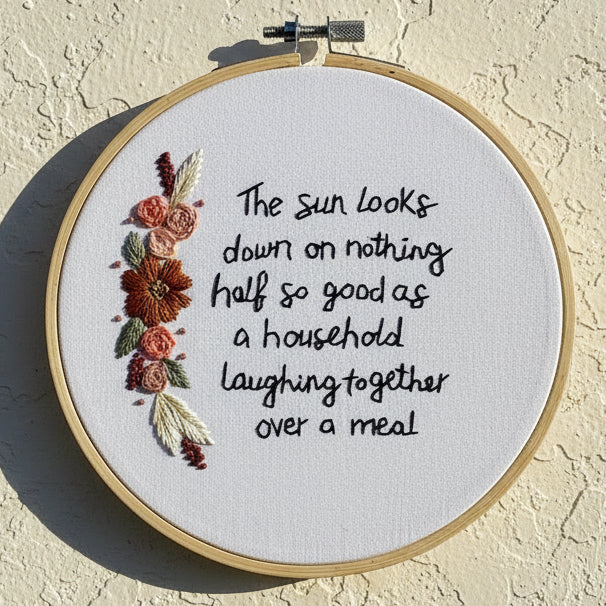 Embroidery hoop with floral design and text on a beige wall