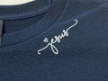 Navy blue shirt with 'Jesus' on it in white on a plain background