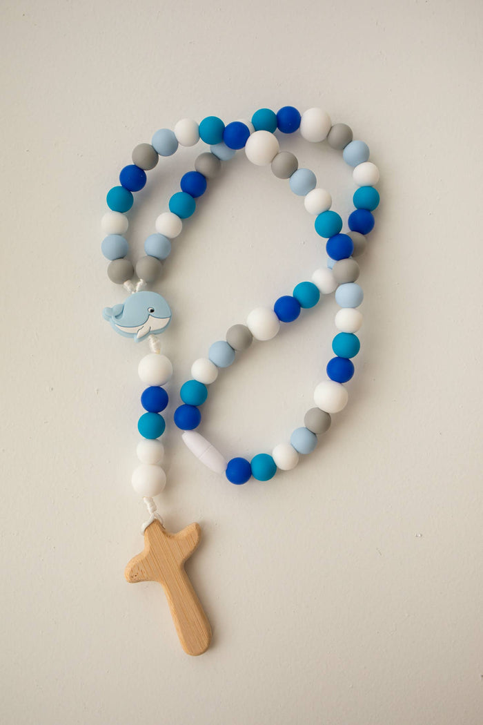 Rosary with blue, gray, and white beads and wooden cross and whale pendant on a light background