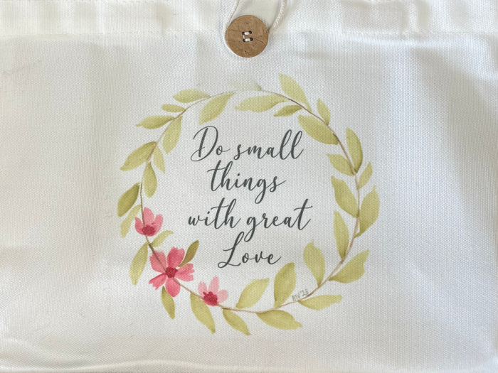White tote bag with floral design and text on a textured surface