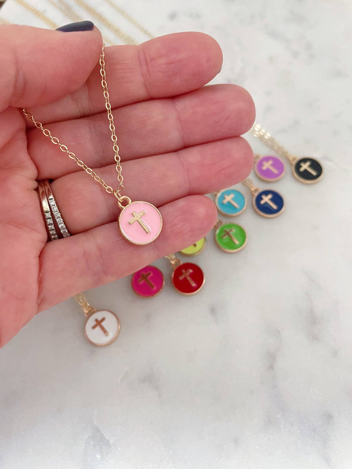 Hand holding a gold necklace with a pink pendant, colorful pendants on a marble surface.