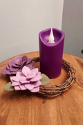 Purple candle on a wooden table with a succulent wreath.